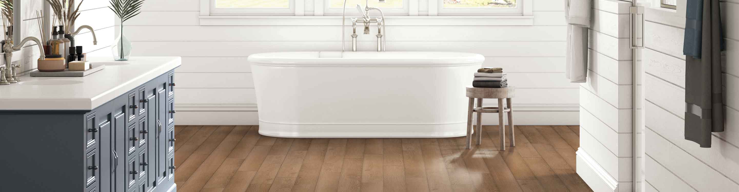 wood-look vinyl flooring in modern farmhouse bathroom with blue vanity, white shiplap walls and deep soak tub